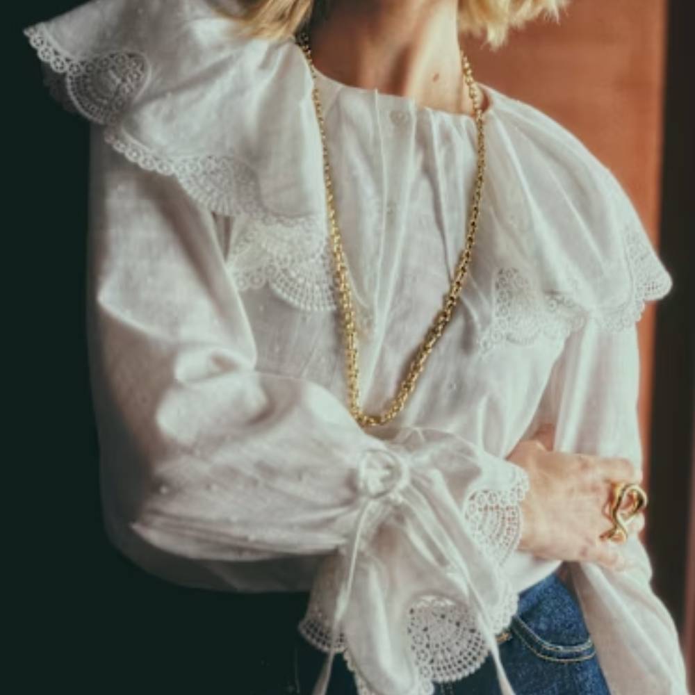 A female model wearing a feminine, frilly blouse from Sezane.