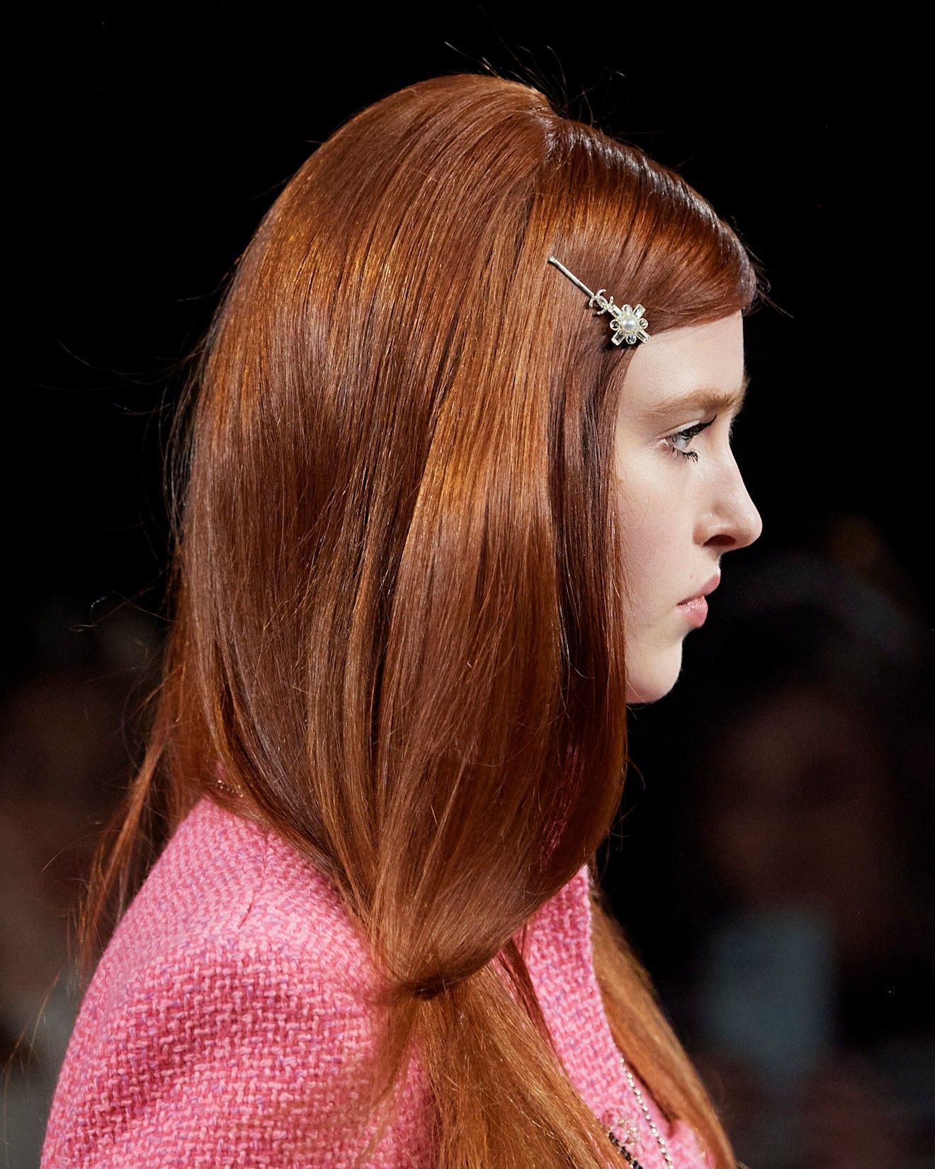 A model with red hair and a silver pin at the front in a pink blazer