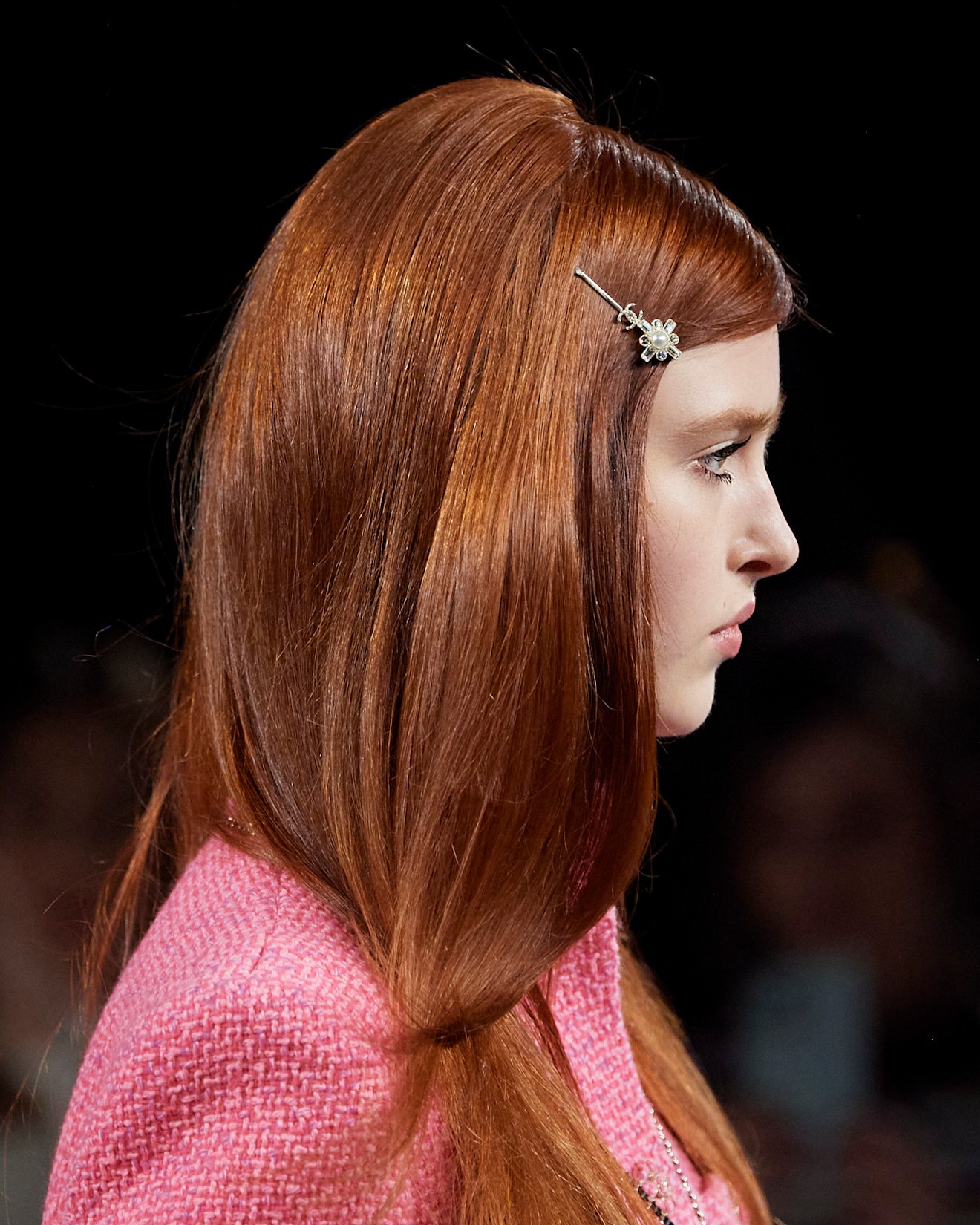 A model with red hair and a silver pin at the front in a pink blazer