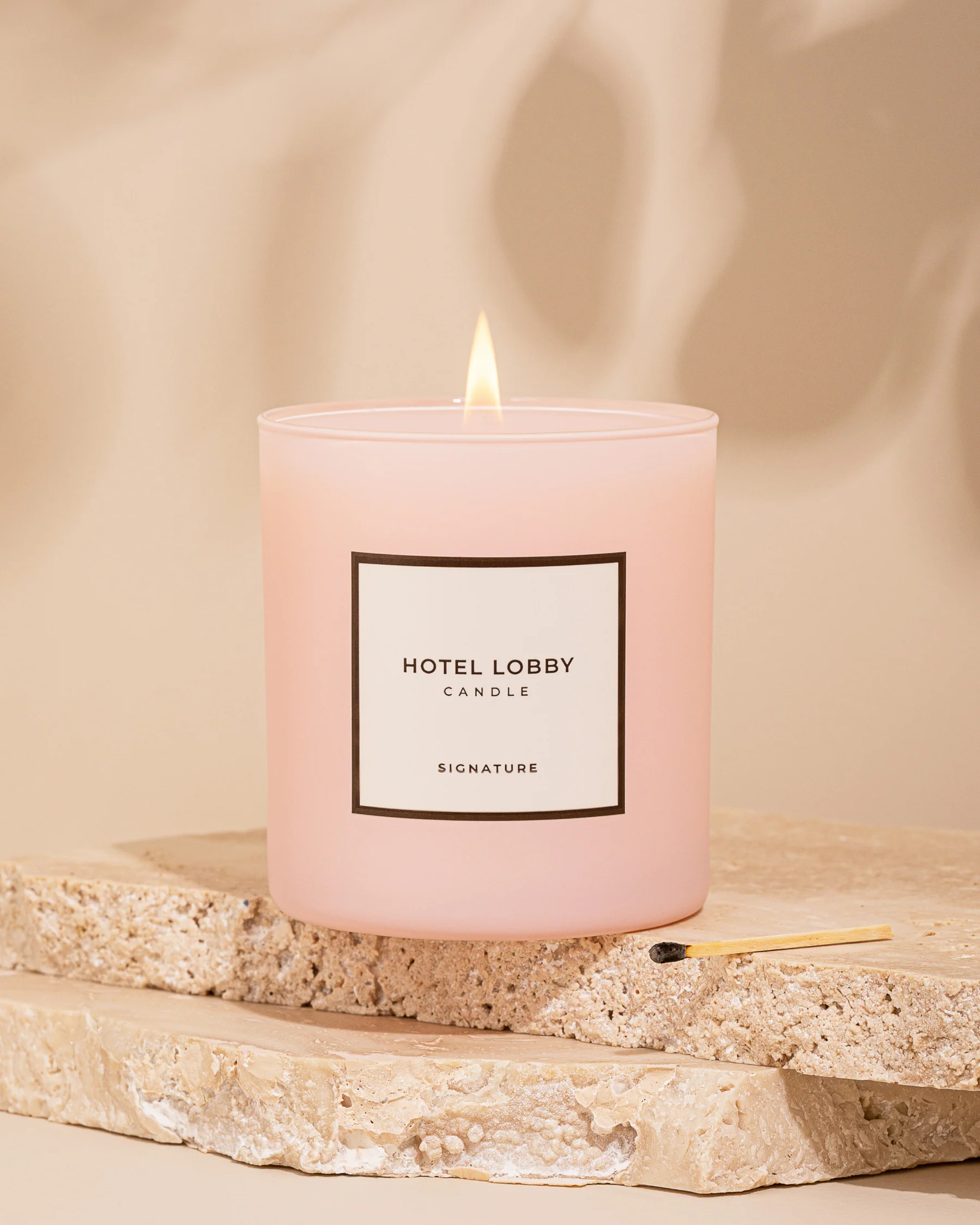 A pink Hotel Lobby Signature candle sits on a piece of rock