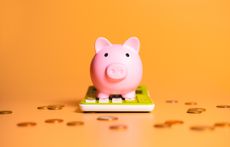 pink piggy bank sitting on a calculator with pennies scattered around it and an orange background