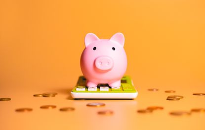pink piggy bank sitting on a calculator with pennies scattered around it and an orange background