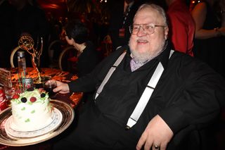 George R. R. Martin is very happy to be at a table with cake.