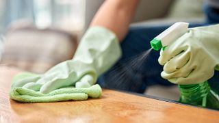 Spraying cleaner on wooden table with cloth