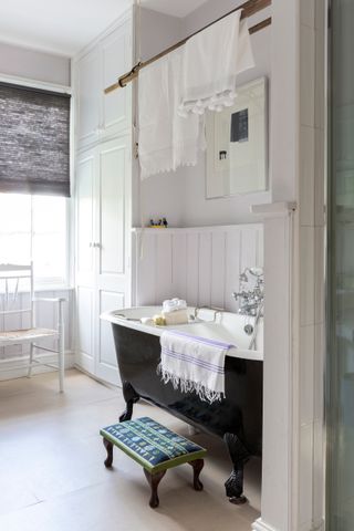 A bathroom in a Regency townhouse with black freestanding bathub and white paneling