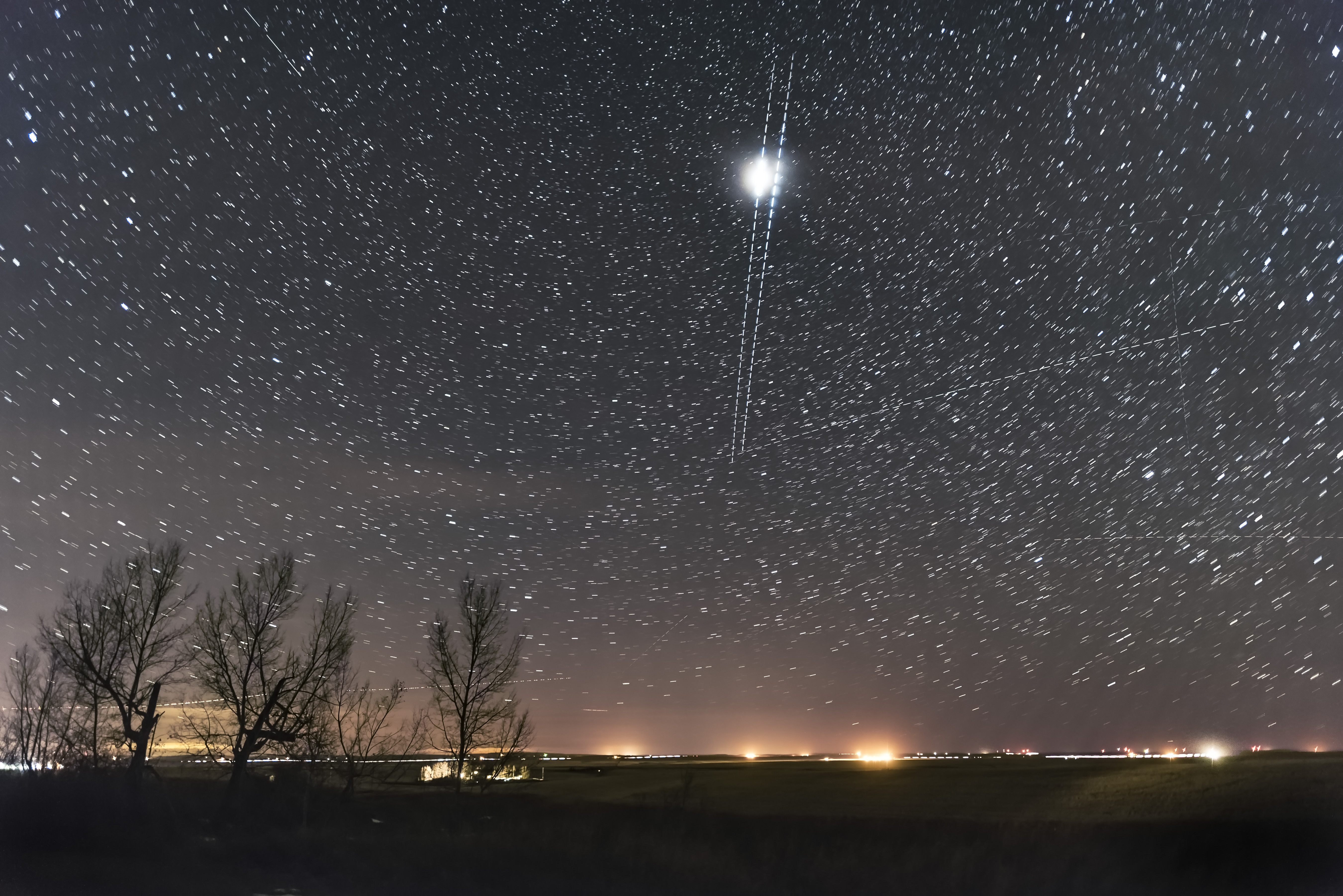 against the starry night sky, two streaks of light pass from top to bottom with a center section appearing much brighter than the rest of the streaks