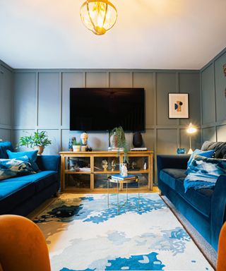 Blue velvet sofas next to a white and blue rug and a mounted TV