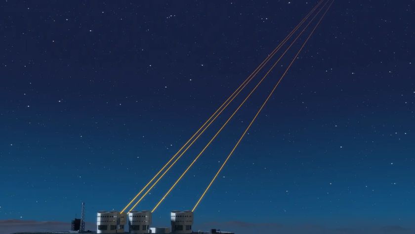 A series of small round buildings at the bottom left of the image with four yellow lasers pointing into the top right of the image over a dark blue night sky. 