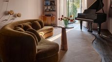 Image of an organically shaped rug in a living room with an ochre yellow curved sofa, a small table in front of it, and a piano in the corner.