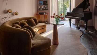 Image of an organically shaped rug in a living room with an ochre yellow curved sofa, a small table in front of it, and a piano in the corner.