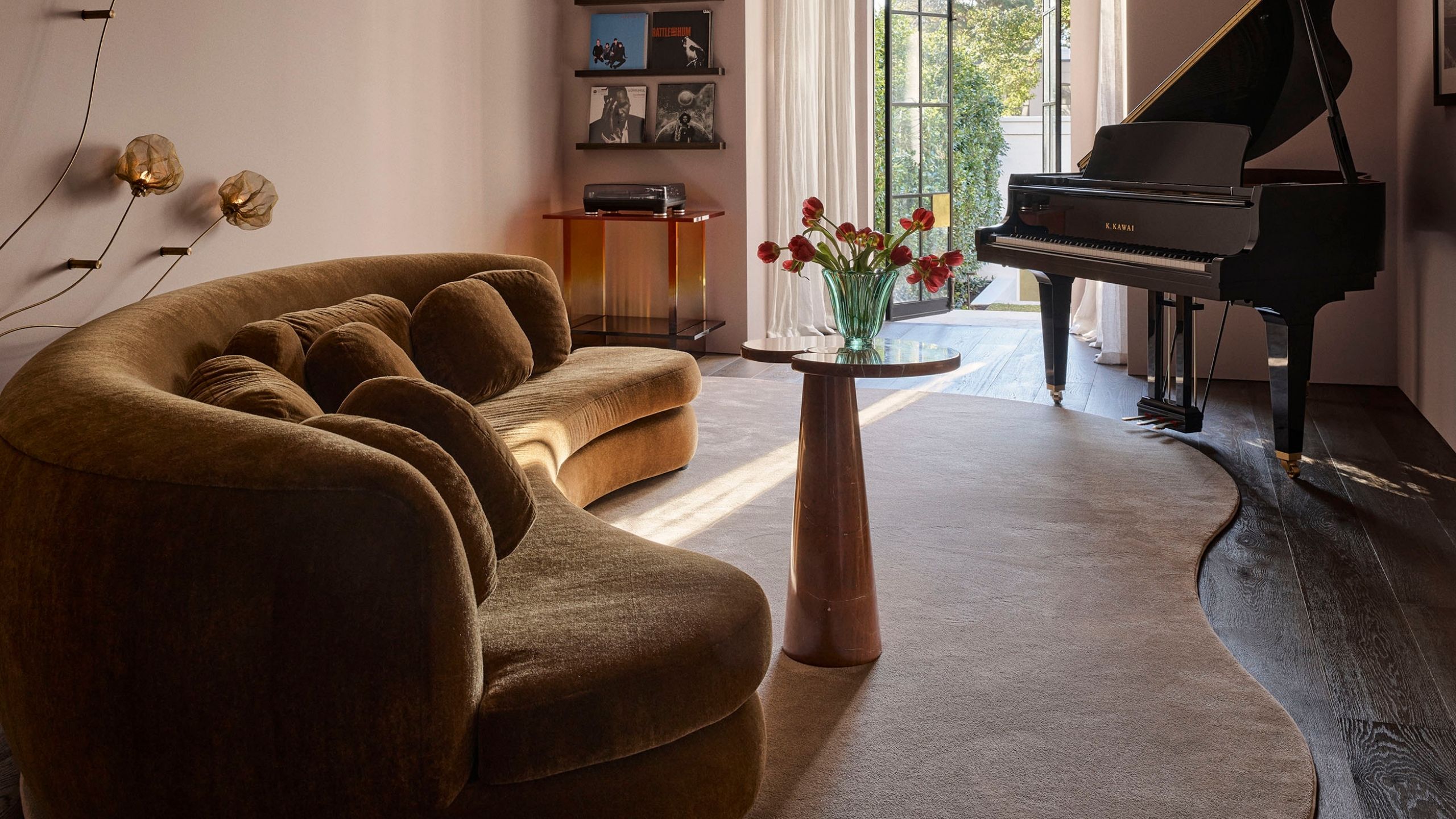 Image of an organically shaped rug in a living room with an ochre yellow curved sofa, a small table in front of it, and a piano in the corner.