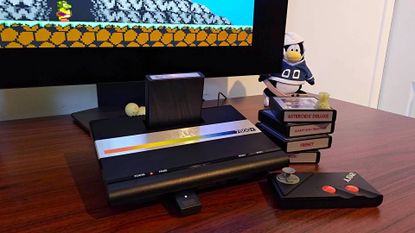 Atari 7800+ console on woodgrain desk next to cartridges, controller and plugged into LG monitor with Bentley Bear&rsquo;s Crystal Quest gameplay on screen