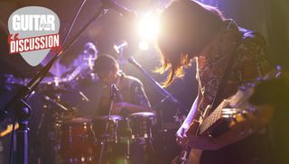 A woman plays the guitar (right) in front of a drummer