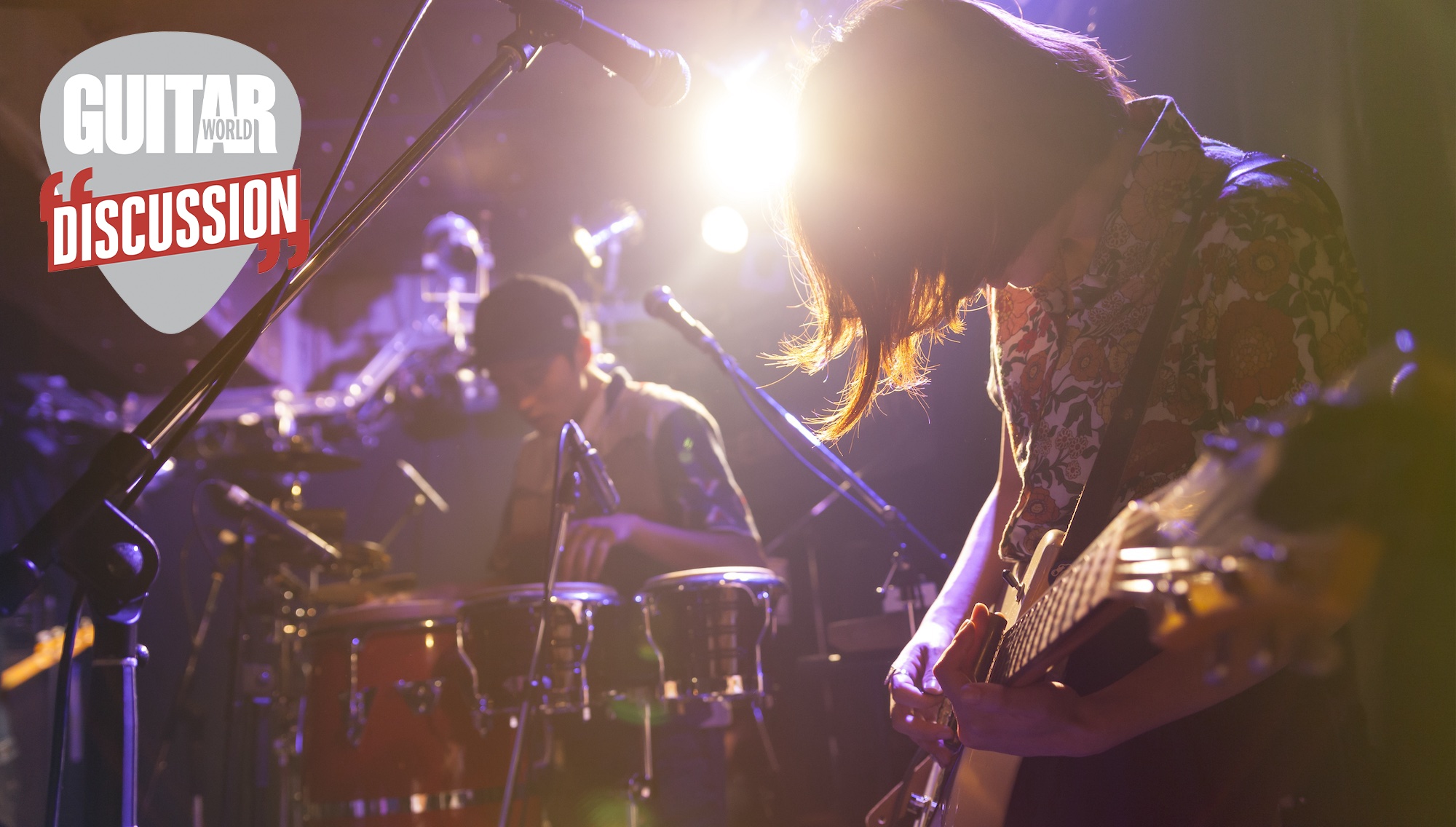 A woman plays the guitar (right) in front of a drummer