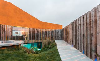 Enclosure made from railway sleepers protects the hilltop home from the wind