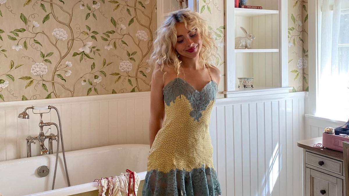 Photo of Sabrina Carpenter standing in a bathroom wearing a yellow and blue dress