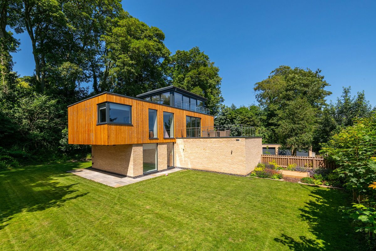 The garden is over hanged by the roof of the second floor and also has a light brown brick wall separating it from the drive