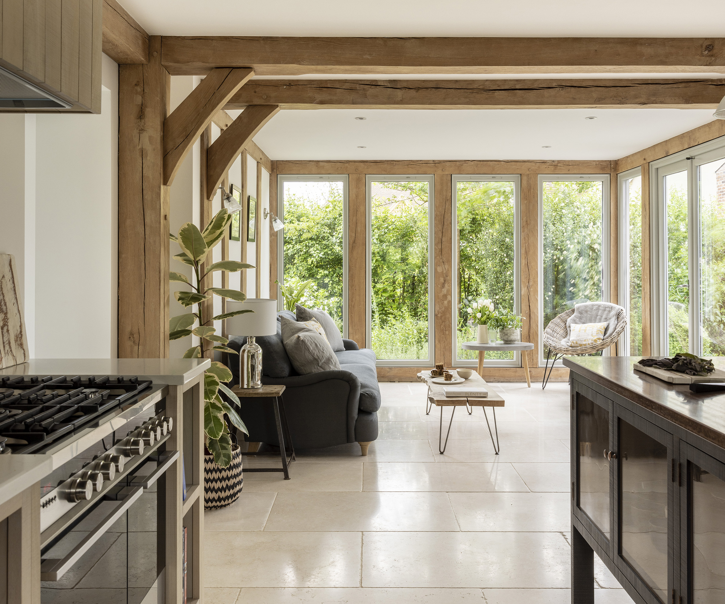 An open plan kitchen and living room in an oak frame home with exposed beams and tiled floor