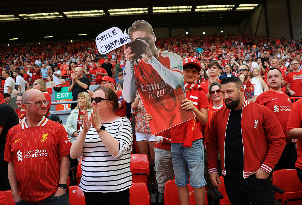 A Liverpool fan holds a carboard cutout of Arsenal player Martin Odegaard holding a camera with the speech bubble reading "Smile Champions" prior to the Premier League match between Liverpool FC and Arsenal FC at Anfield on May 11, 2025 in Liverpool, England.