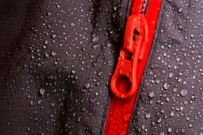 How to re-waterproof your cycling jacket image se up of water beading off black fabric with a red zip in the middle of the image
