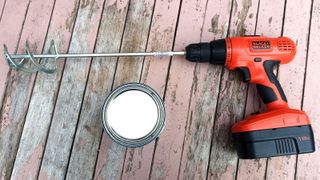 Cordless drill with mixer paddle next to tin of paint on painted wooden table
