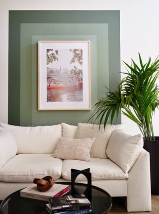 Three different shade of green framing some artwork on a wall behind a cream sofa and black coffee table
