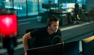Jake Gyllenhaal sitting at his 911 station, taking a call in The Guilty.