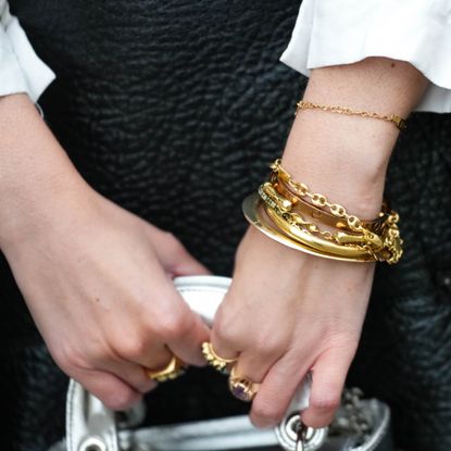 Alba Garavito Torre wears gold bracelets, a white blouse with big from Peter Pan collar and lantern sleeves, a black long wool coat, a black shiny leather short skirt, a silver shiny leather Lady D-Light handbag from Dior, during a street style fashion photo session, on November 05, 2022 in Paris, France. 