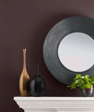 white mantel with dark purple wall, round mirror and decorative items