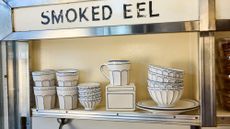 Russ & Daughters x West Elm white ceramic serveware lined in blue pictured atop a mid-century style shelf framed in chrome