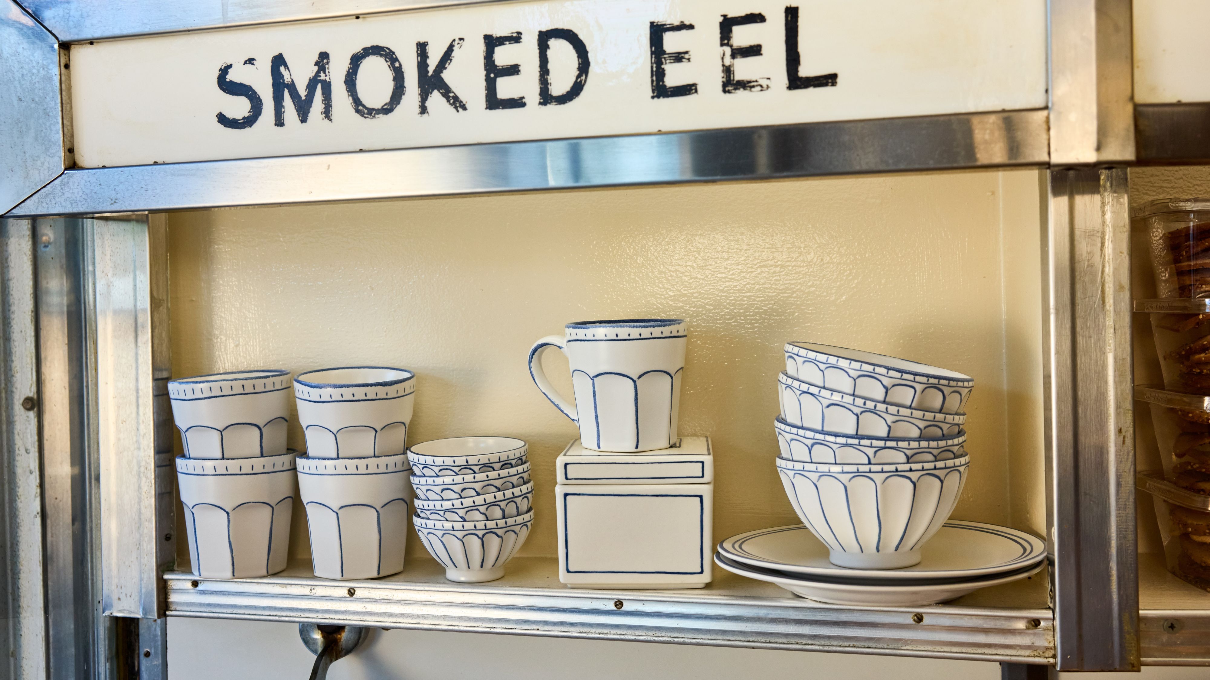 Russ &amp; Daughters x West Elm white ceramic serveware lined in blue pictured atop a mid-century style shelf framed in chrome