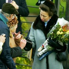 Princess Anne wearin ga blue coat with fur trim holding a bouquet of flowers and talking to fans outside on Christmas Day