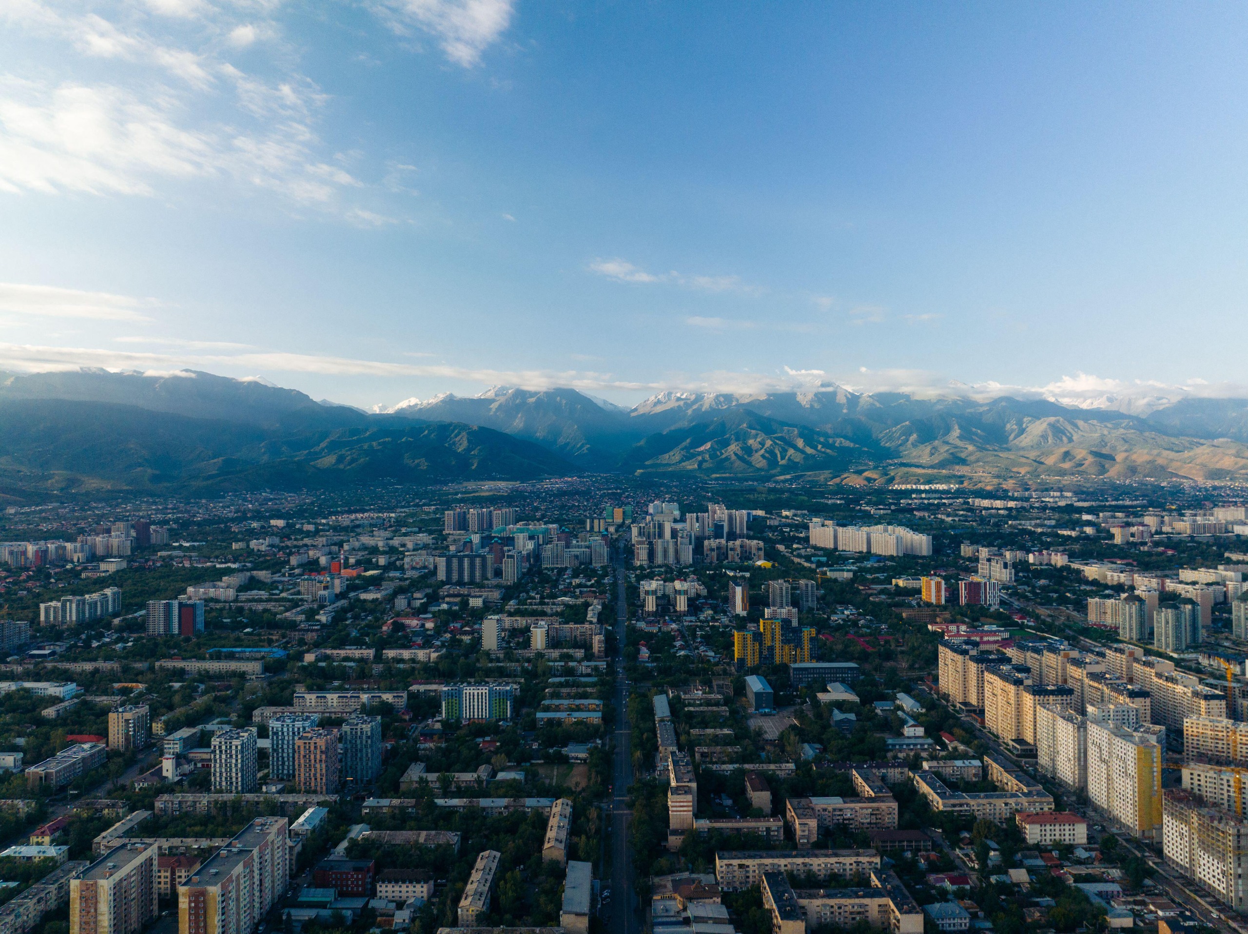 An aerial view of the streets of almaty, with soaring mountains beyond