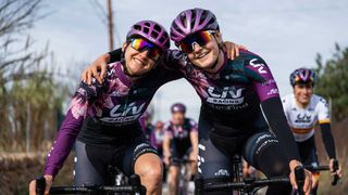 Two female cyclists smiling at the camera with one arm around the other