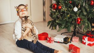 A boy and a cat sit under a Christmas tree opening presents