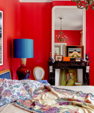 Fiery red walls with blue cobalt lampshade and mirror of fireplace in eclectic bedroom design