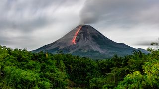 A volcano with lava running down its side. The volcano is surrounded by lush forest.
