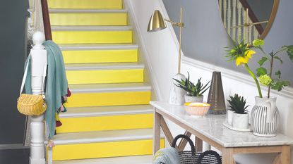 A yellow-painted staircase with a white bannister leading to a hallway with a marble-top console table