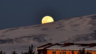 a bright full moon rises behind a snow-covered mountain