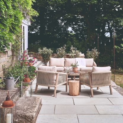 A garden with a wooden garden lounge set with beige cushions and woven string detailing