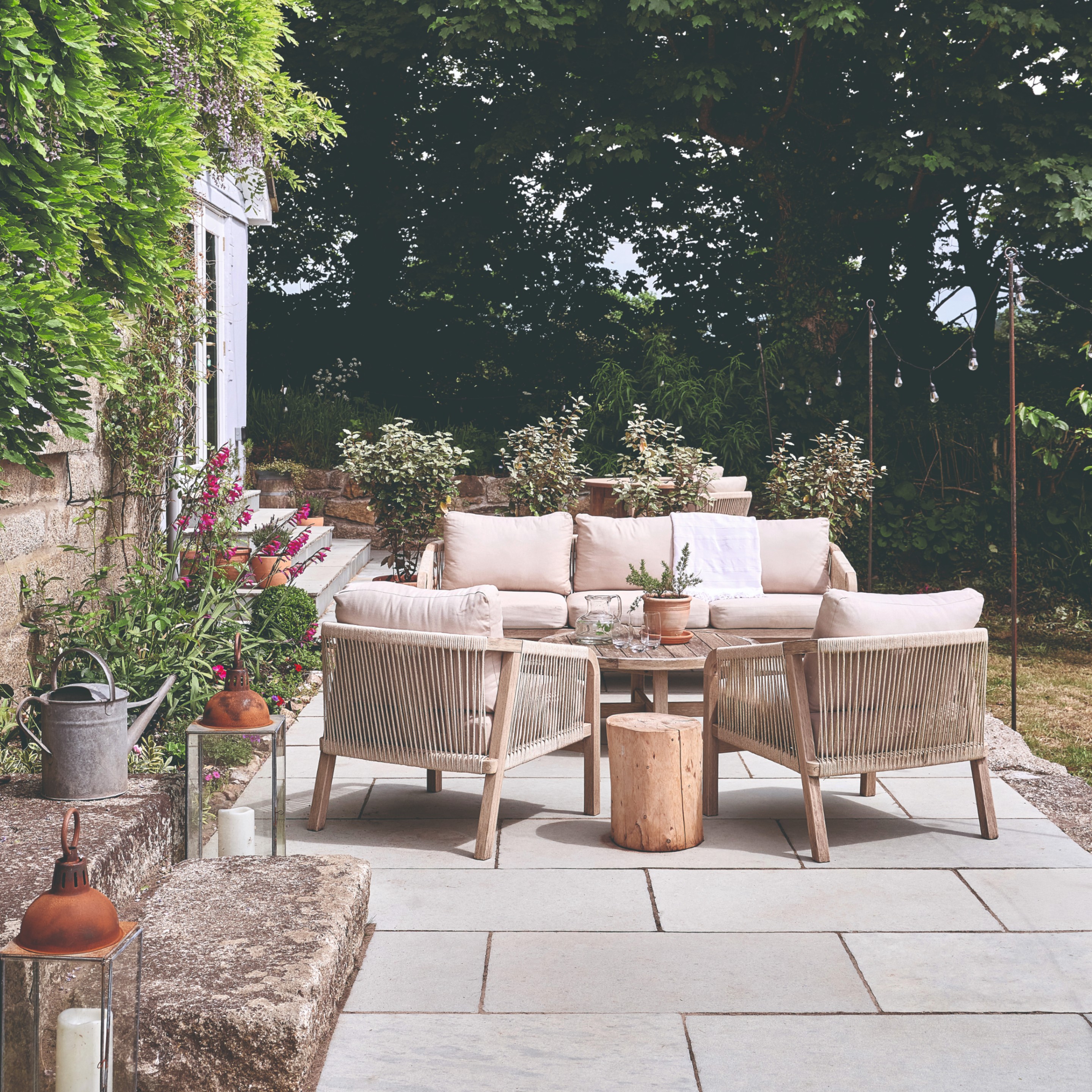 A garden with a wooden garden lounge set with beige cushions and woven string detailing 