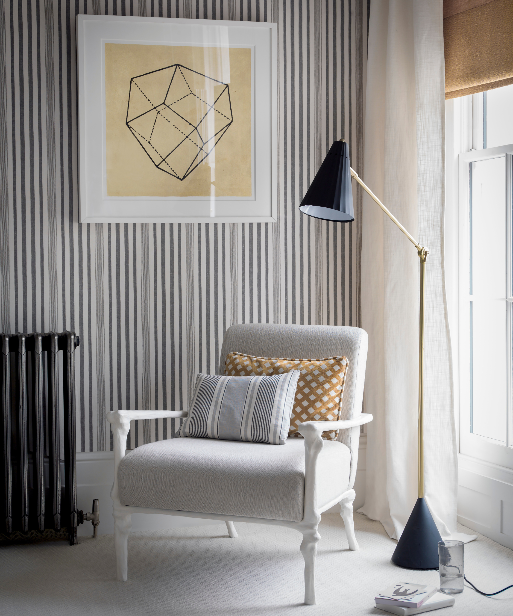 a chair in a corner of a room with a floor lamp, striped wallpaper, and artwork on the walls