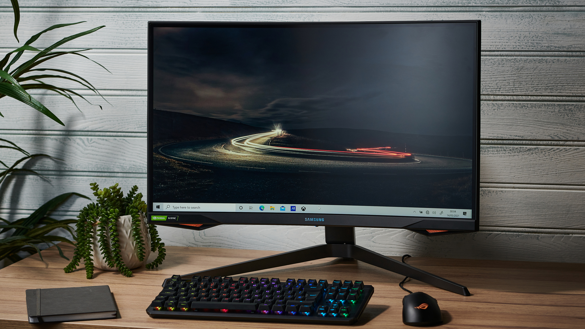 En Samsung Odyssey G7 står på ett träfärgat skrivbord med en mörk bakgrundsbild på skärmen.