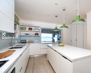 A kitchen with white, handless cabinetry and green pendant lights over the island