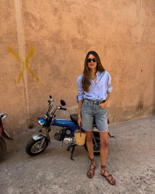 An influencer wearing relaxed denim shorts with a blue shirt and sandals.