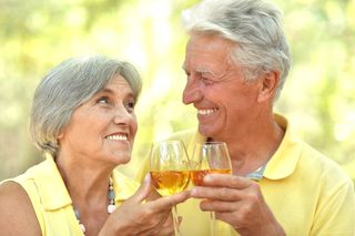 An older couple toasts with glasses of white wine