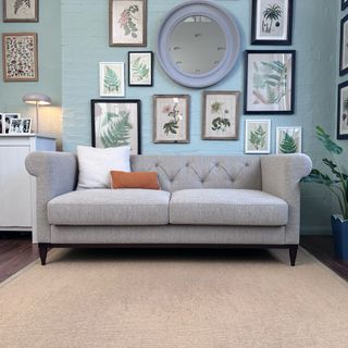 Swyft Chesterfield sofa in grey in a living room with a blue wall and frames on the wall