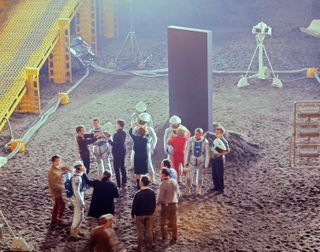 Actors and crew from "2001: A Space Odyssey" relax after completing photography in a set representing a huge lunar pit where a strange black monolith has been excavated.