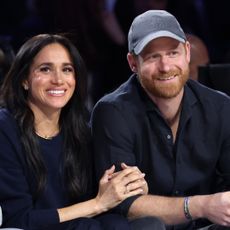 Prince Harry and Meghan Markle sitting next to each other in black outfits