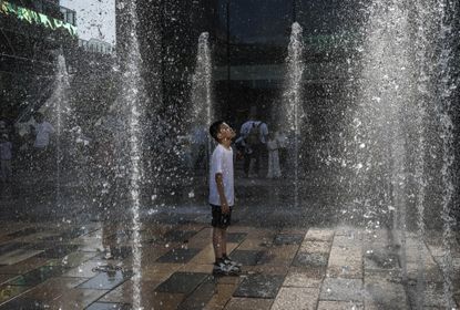 A young boy in China stands in a fountain on a hot day